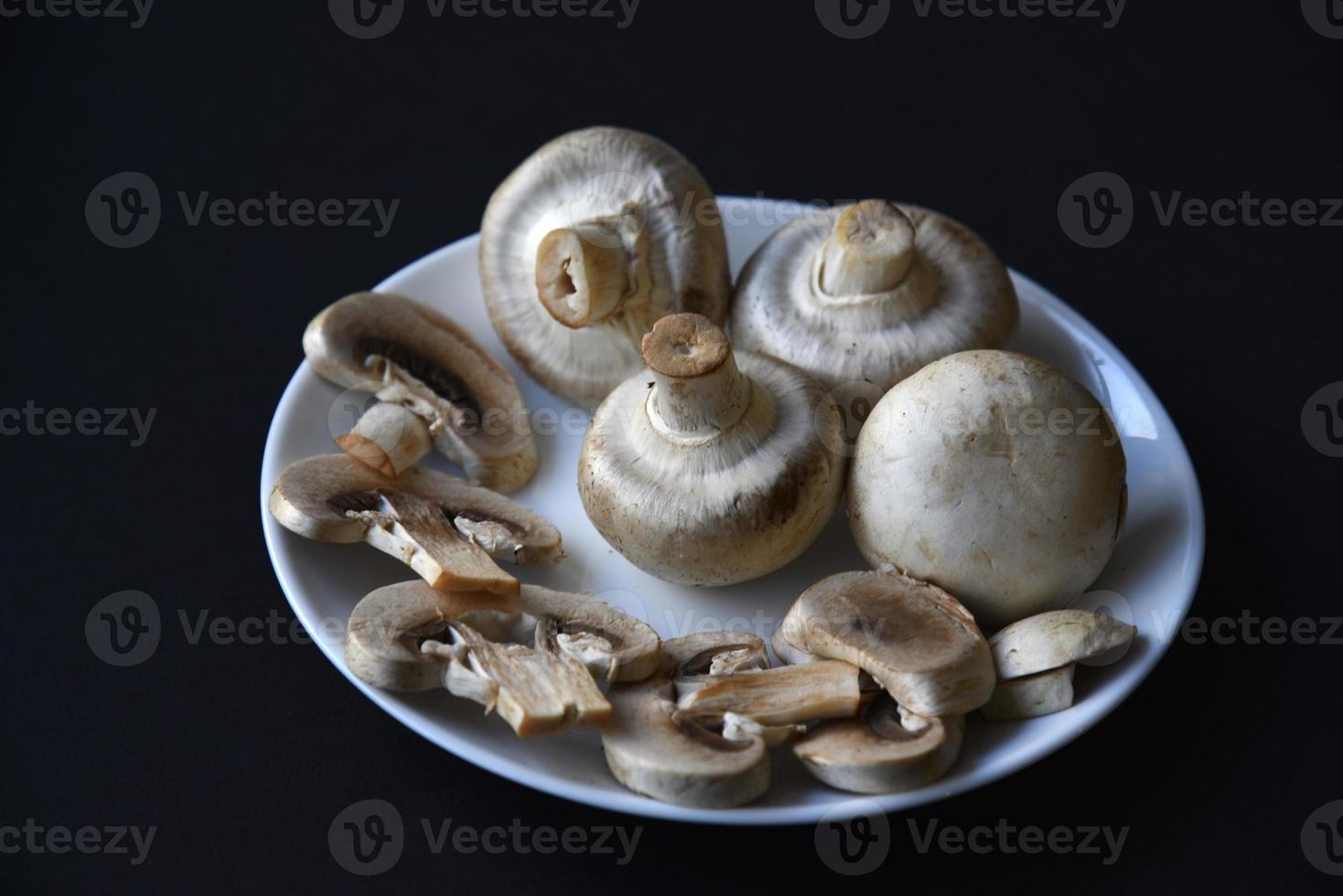 Porcini mushrooms in a white plate on a black background. Fruits of large white champignons close-up. Beautiful mushrooms in a plate. photo