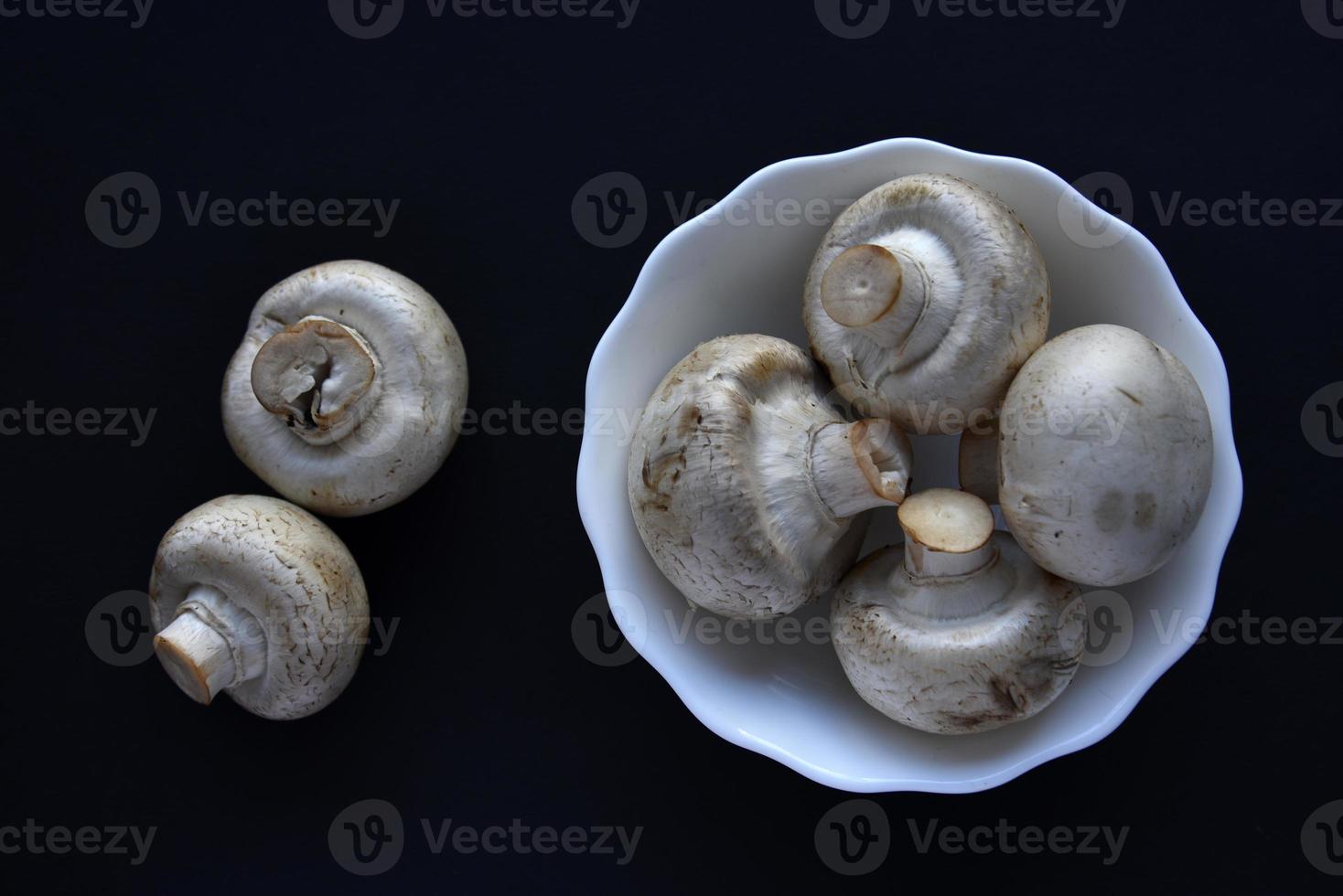 Porcini mushrooms in a white plate on a black background. Fruits of large white champignons close-up. Beautiful mushrooms in a plate. photo
