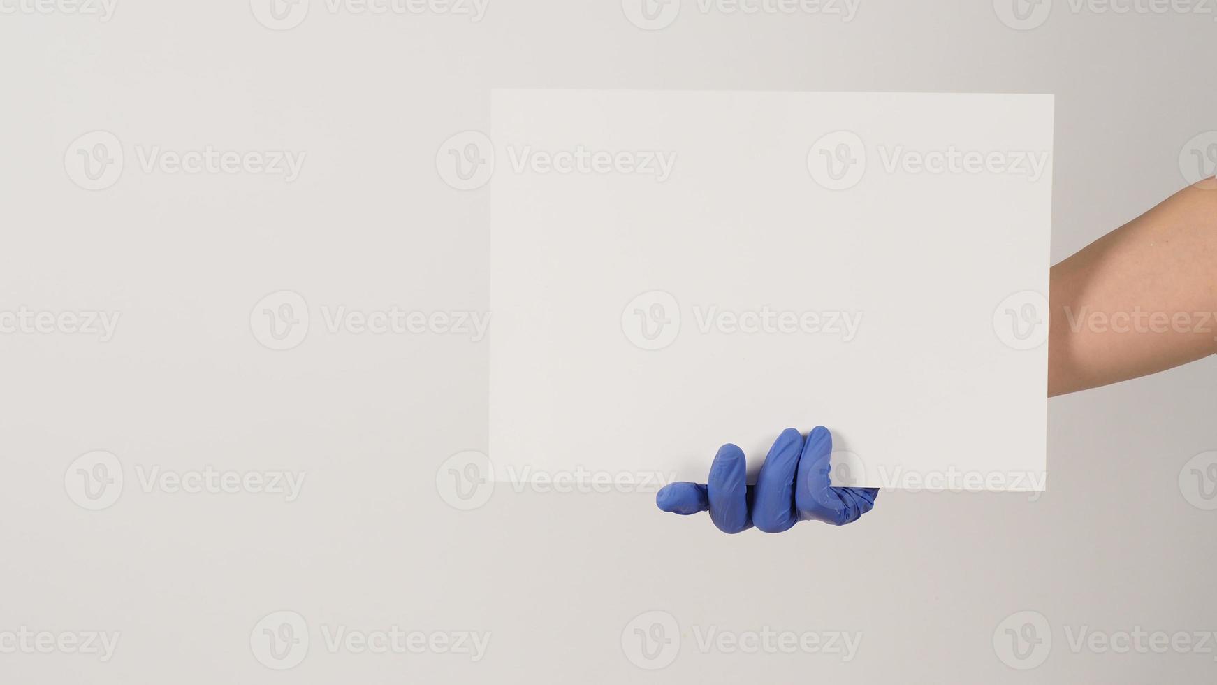 Hand is holding the A4 paper and wear purple latex glove on white background. photo