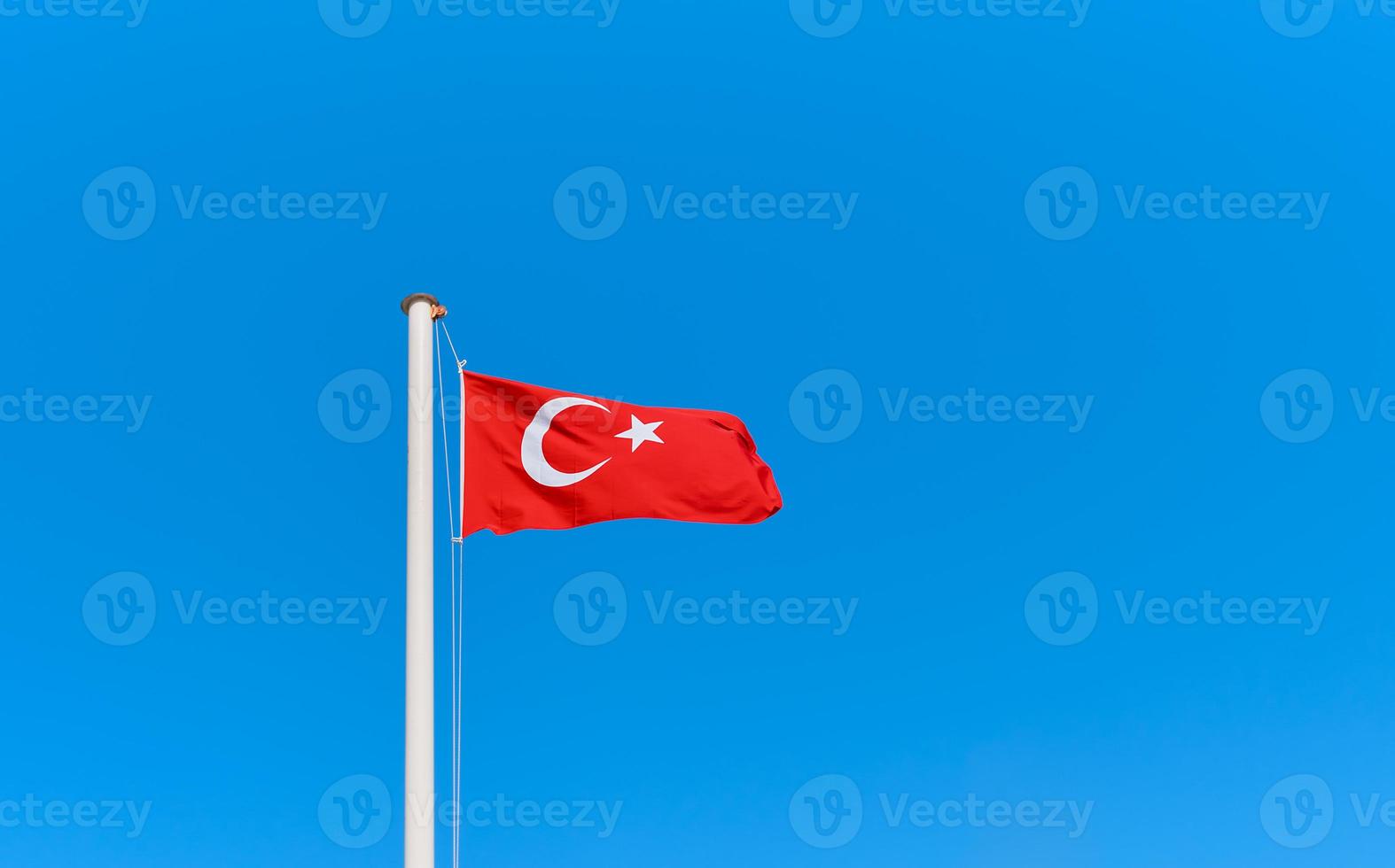 Turkish flag on a flagpole against a clear blue sky with copy space. Idea for background or wallpaper photo