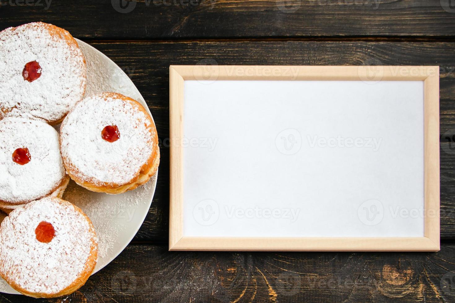 Happy Hanukkah. Empty frame for congratulations text and traditional dessert Sufganiyot on dark wooden background. Celebrating Jewish holiday. photo