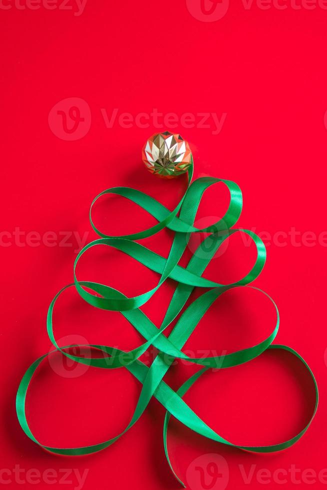 Festive tree made of satin green ribbon on red background. Creative Christmas concept for advertising. photo
