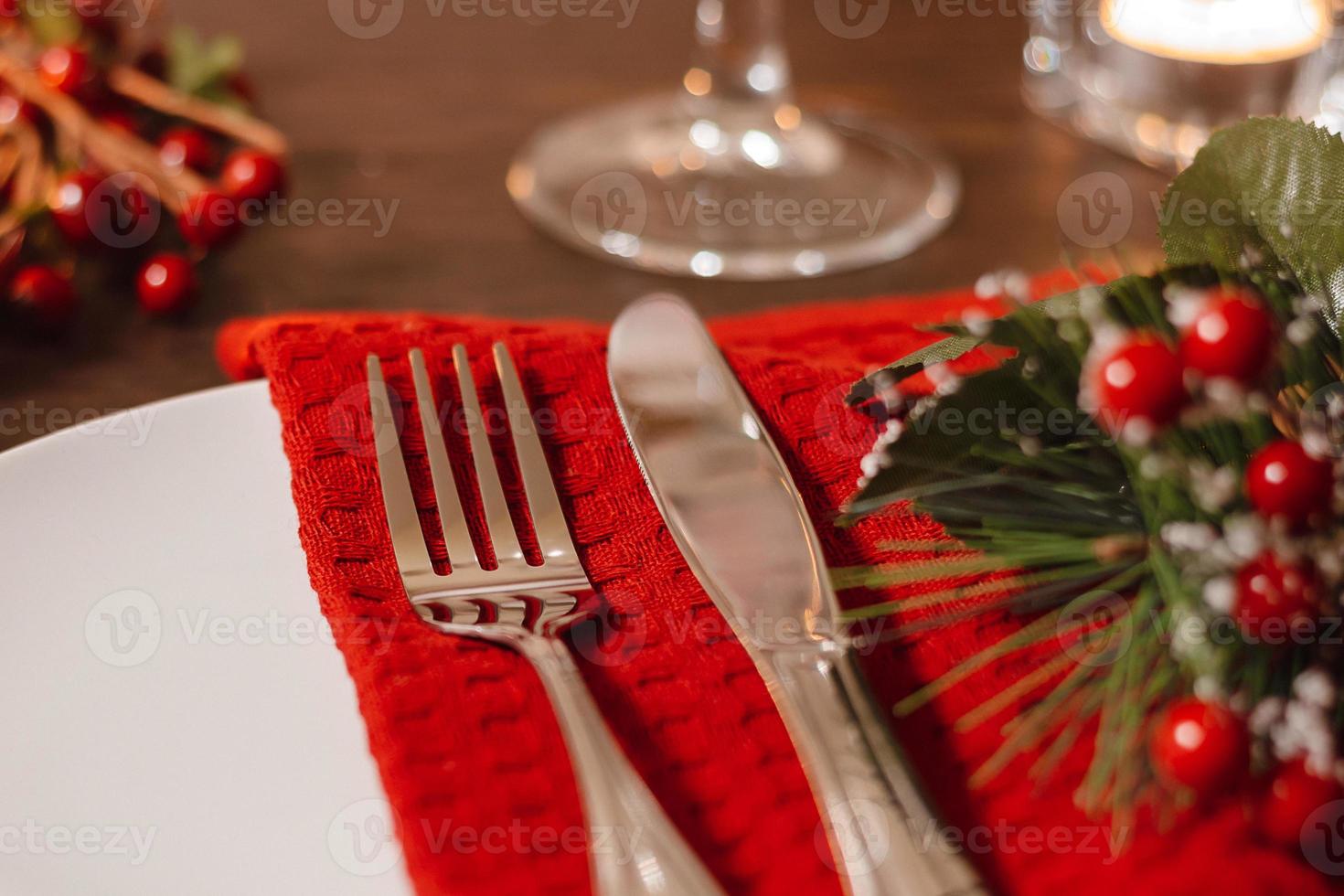 Christmas table setting. Plate and cutlery on napkin. Preparing for festive dinner. Candles burning on table on Christmas Eve. photo