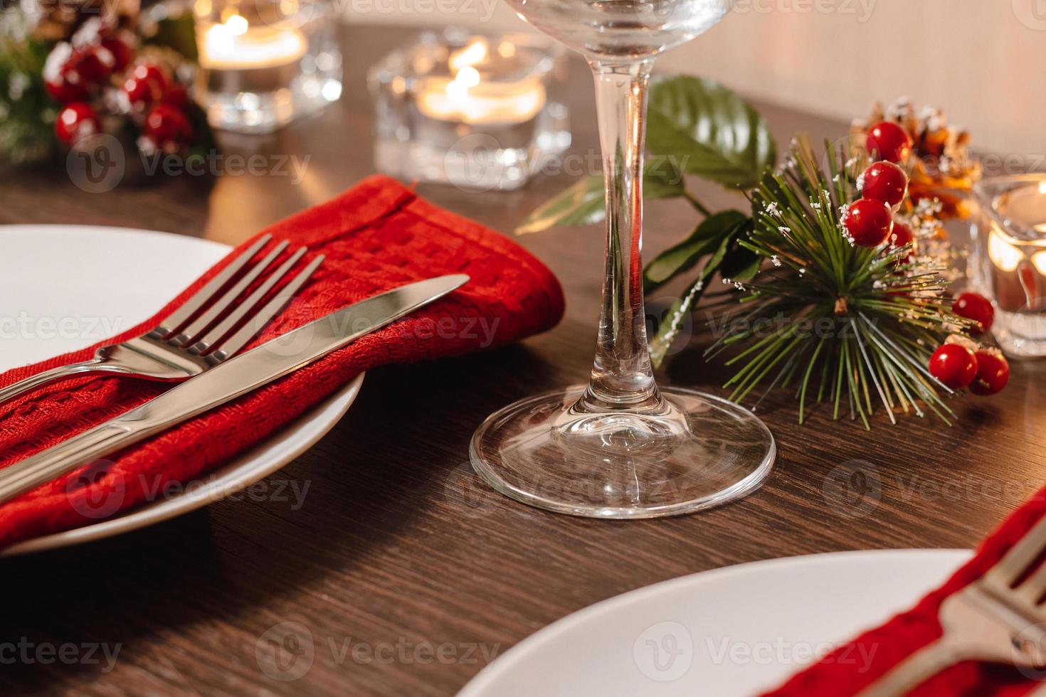 Christmas table setting. Plate and cutlery on red napkin. Candles burning on table on Christmas Eve. Preparing for festive dinner. photo