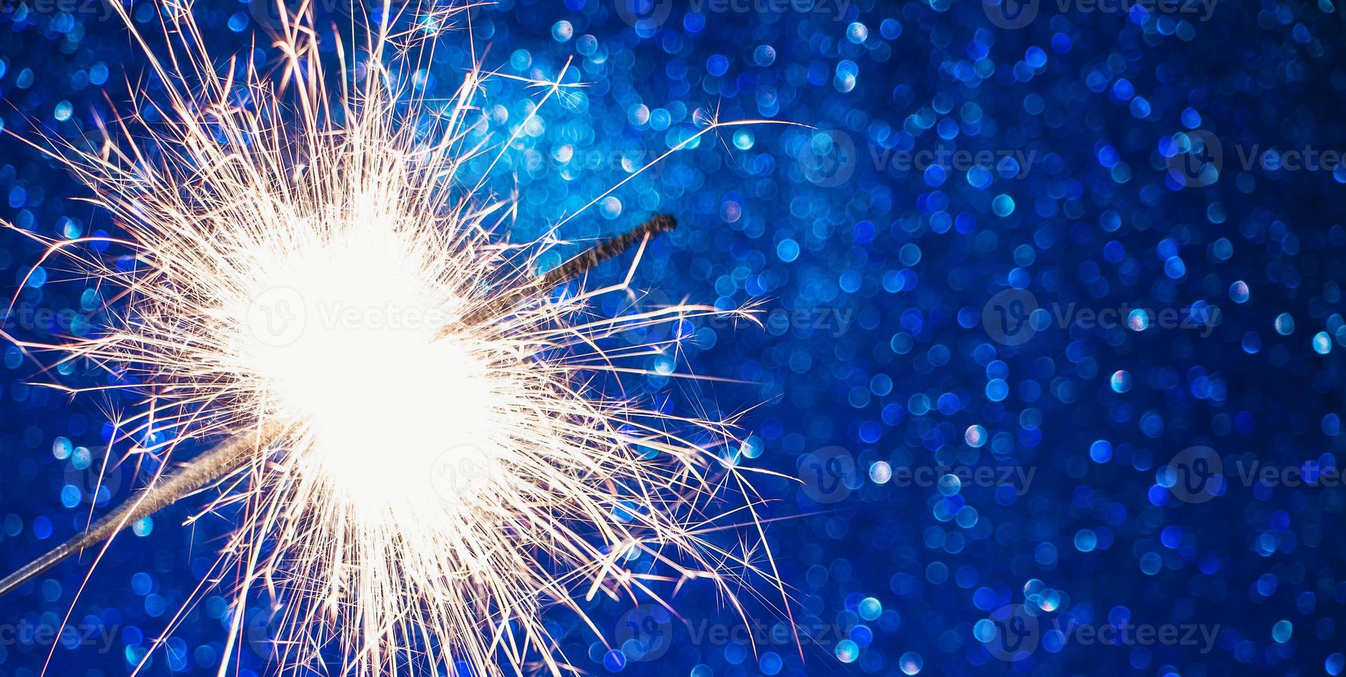 Bright sparkler on blue background. Celebrating New Year and Christmas. Shiny sparks of fire and bokeh. photo