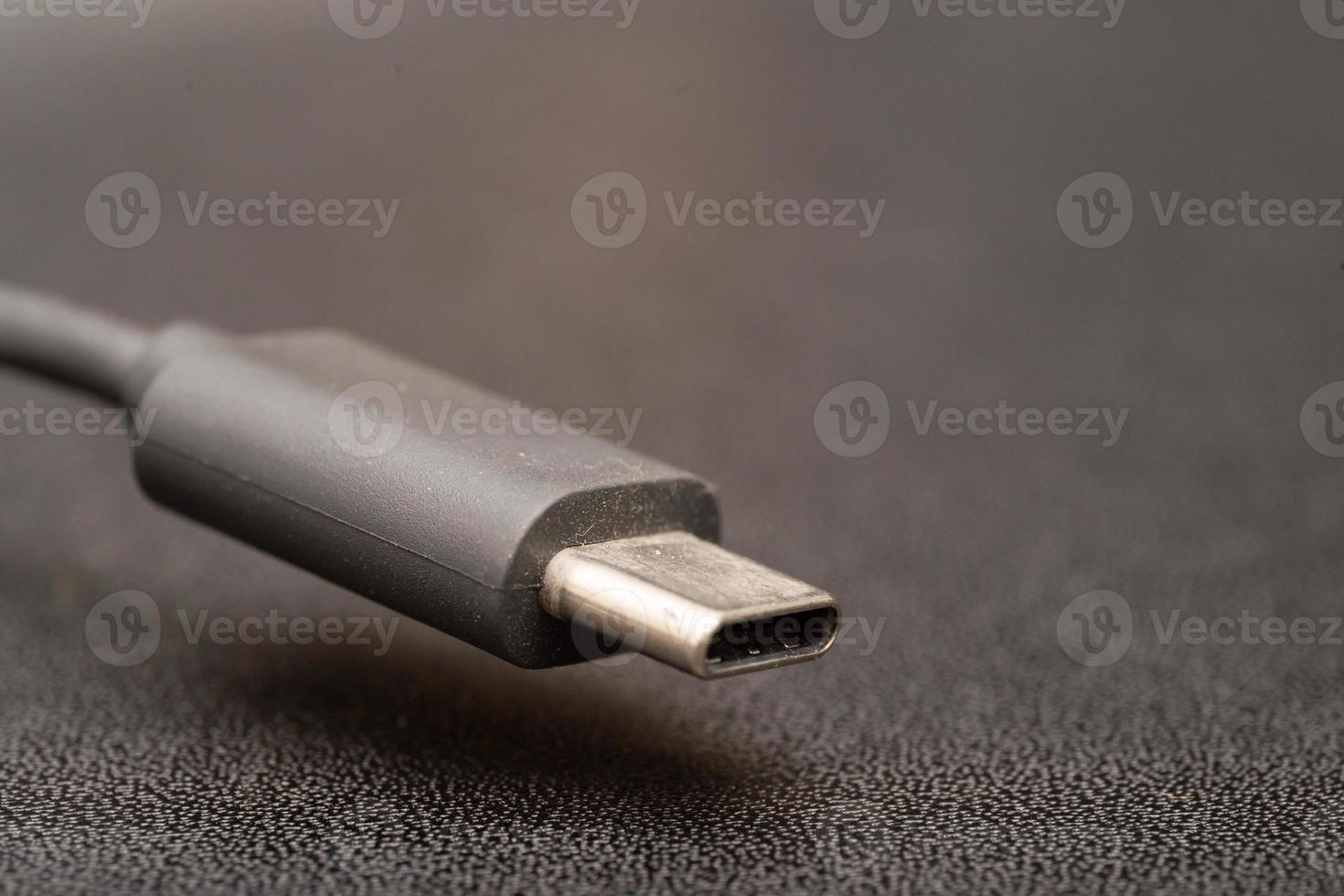 Close up of USB Type C connector with a grey cable on a dark background. Side close-up photo of grey type-c cable.