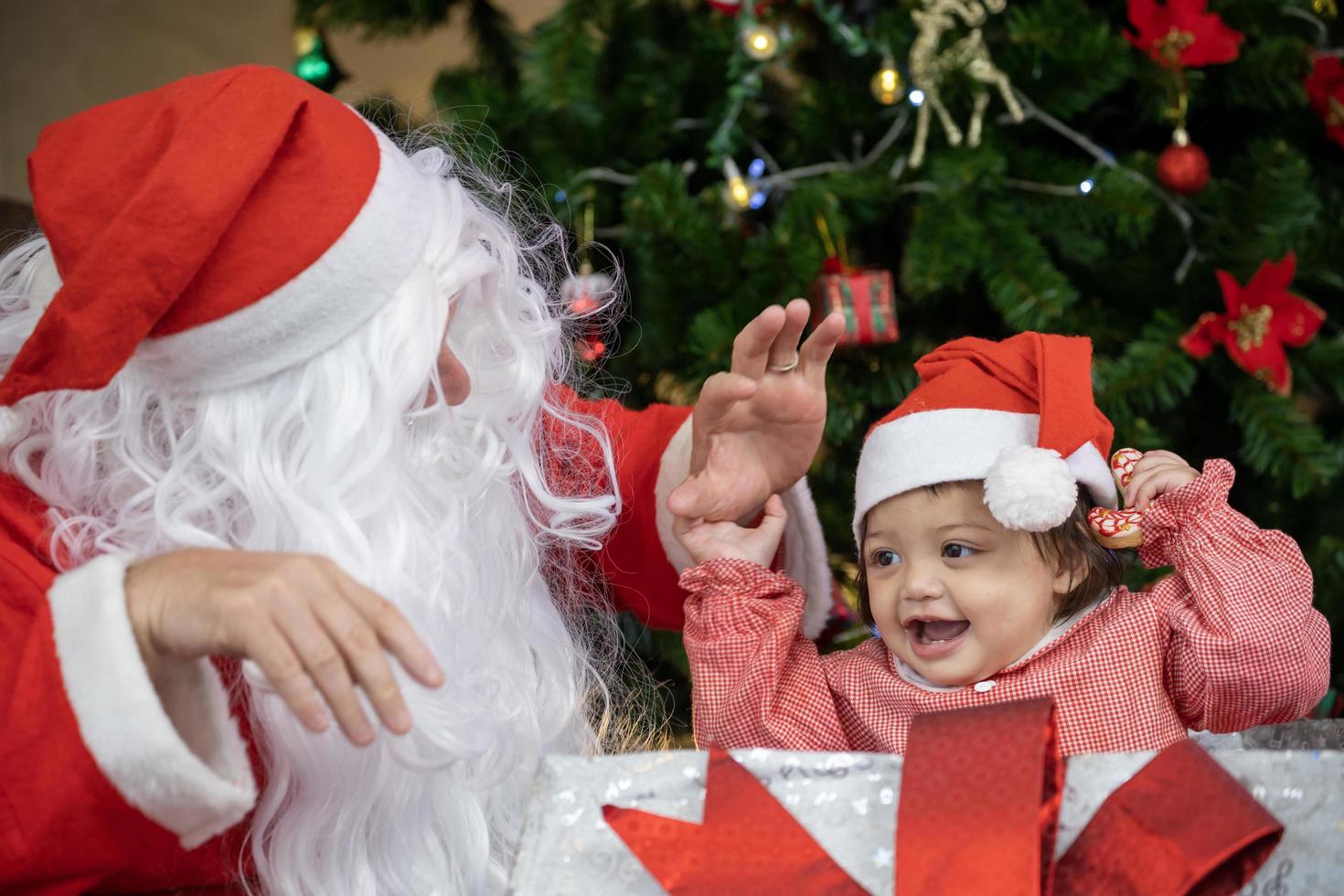 Caucasian baby is playing with present from Santa claus at night by the fully decorated christmas tree for season celebration concept photo