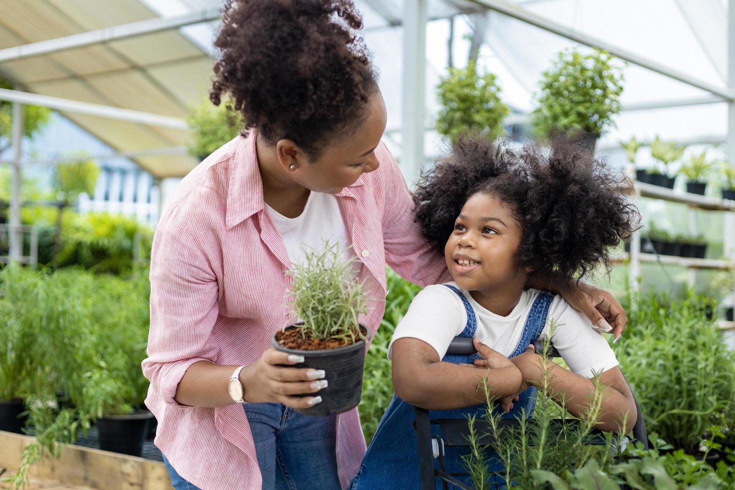 madre africana e hija están eligiendo plantas de verduras y hierbas del vivero del centro de jardinería local con carrito de compras lleno de plantas de verano para la jardinería de fin de semana y el concepto al aire libre foto