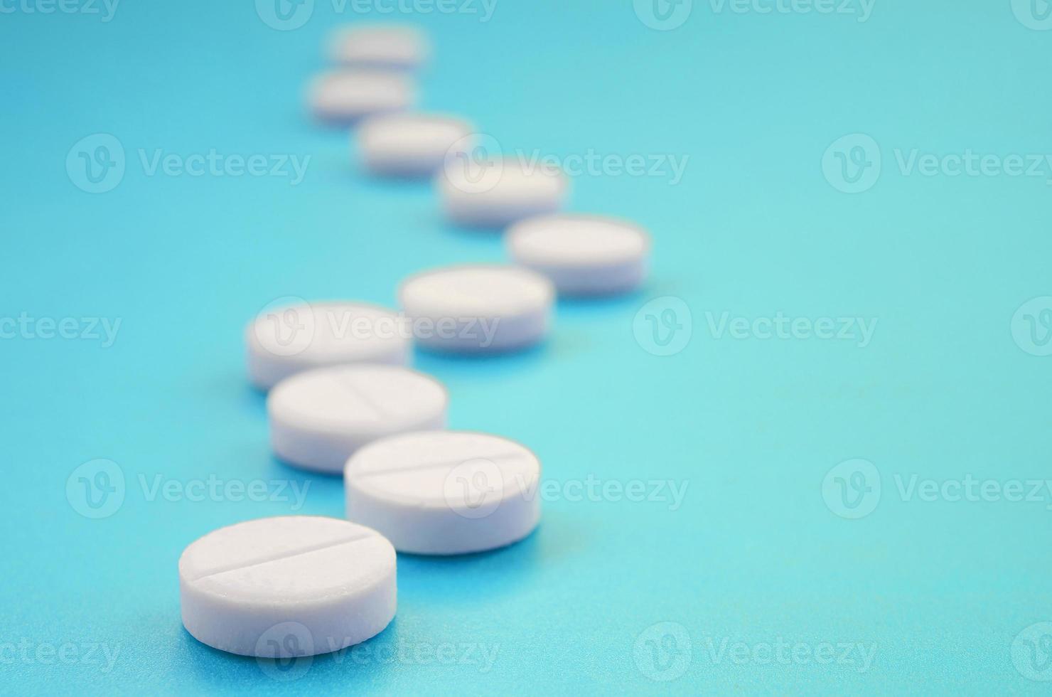 A few white tablets lie on a bright blue background surface. Background image on medical and pharmaceutical topics photo