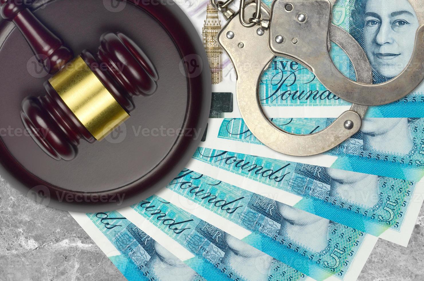 5 British pounds bills and judge hammer with police handcuffs on court desk. Concept of judicial trial or bribery. Tax avoidance photo