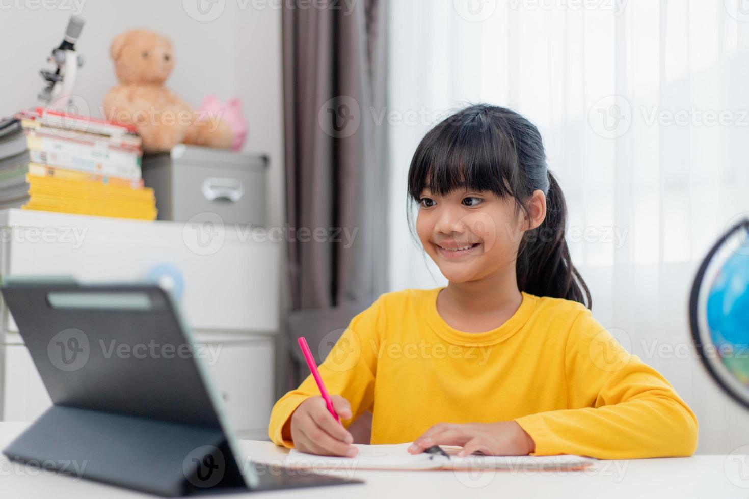 Asian schoolgirl doing her homework with digital tablet at home. Children use gadgets to study. Education and distance learning for kids. Homeschooling during quarantine. Stay at home photo