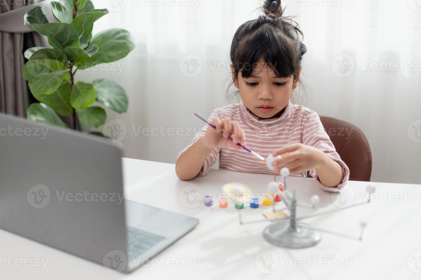 una niña asiática estudia el sistema solar en clase de geografía. mirando el modelo a escala de los planetas foto