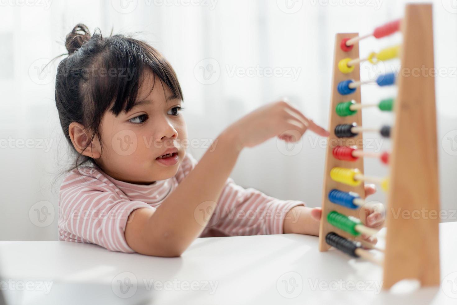 A young cute Asian girl is using the abacus with colored beads to learn how to count at home photo