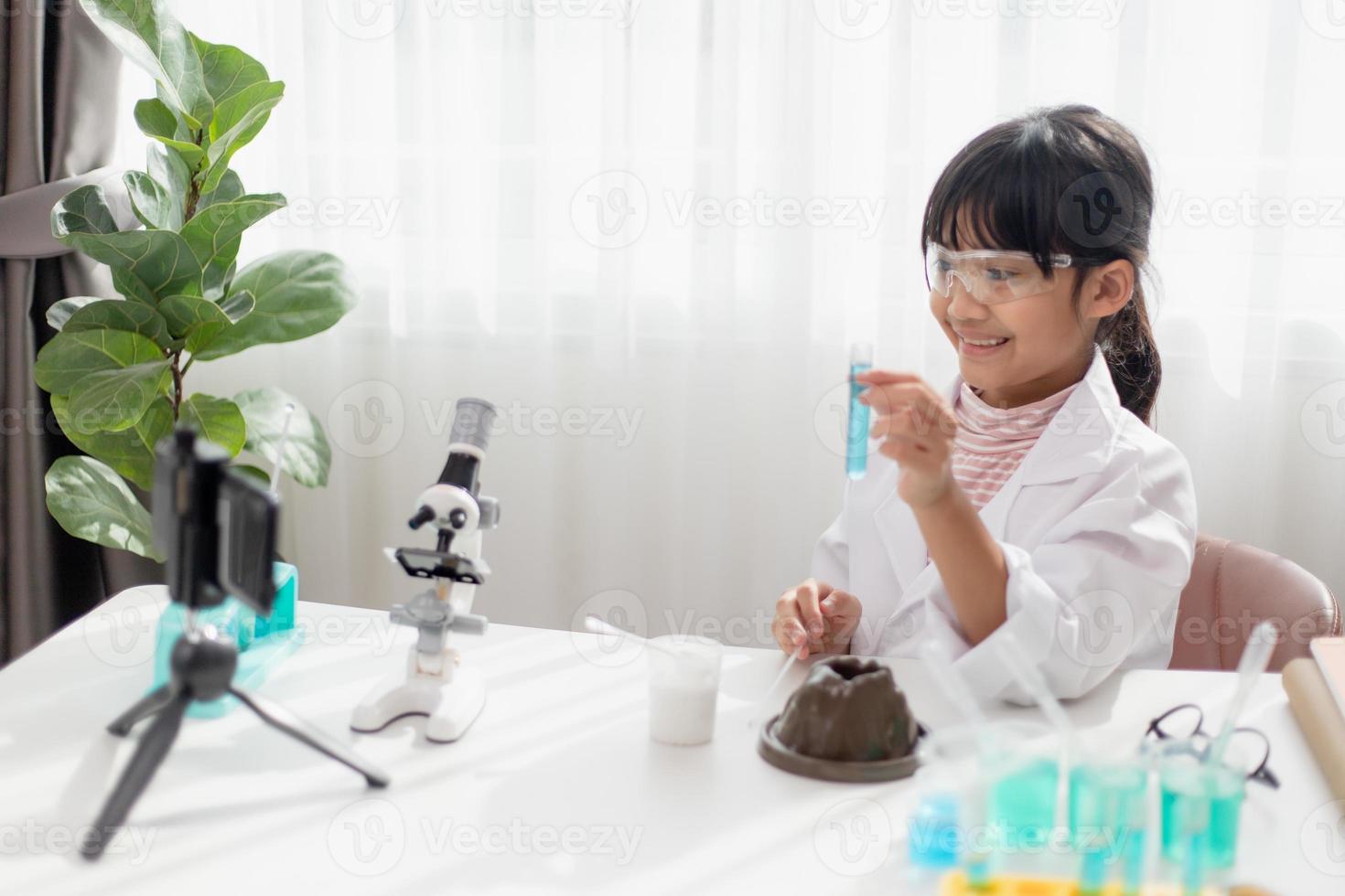 Asian school girl making easy chemistry experiments and recording a video for his followers, Young blogger kid posing in front of camera for vlog, Children make vlog for social media channel concept. photo