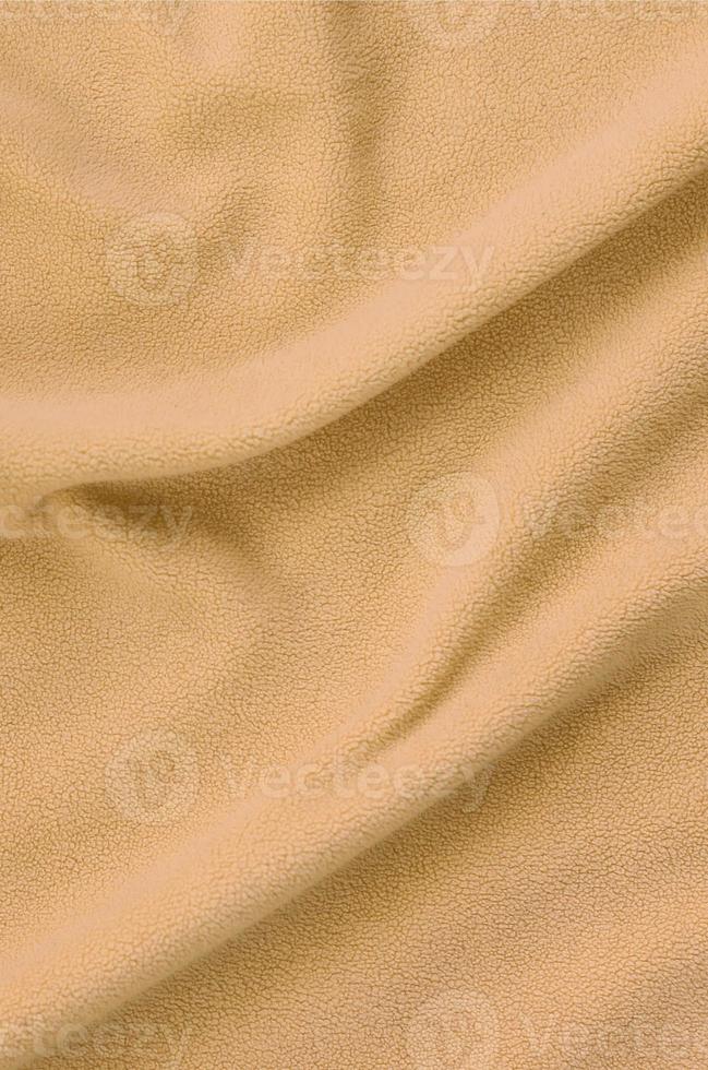 The blanket of furry orange fleece fabric. A background of light orange soft plush fleece material with a lot of relief folds photo