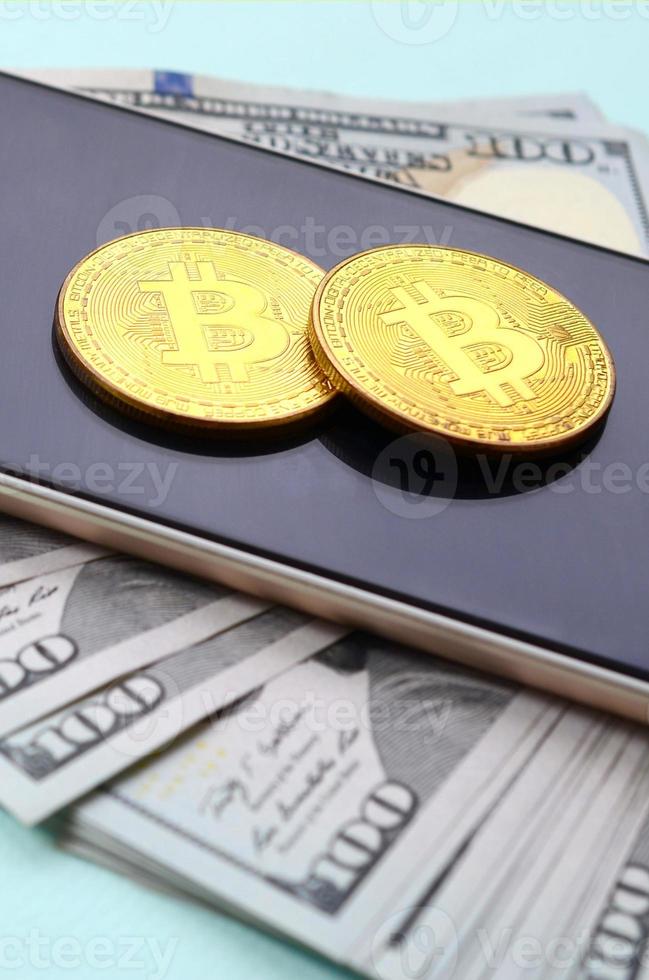 Bitcoins lies on a smartphone and hundred dollar bills on a light blue background photo