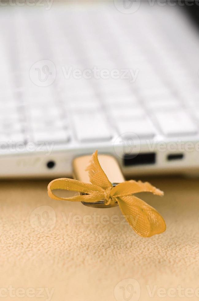 An orange USB flash drive with a bow is connected to a white laptop, which lies on a blanket of soft and fluffy light orange fleece fabric. Classic female design for a memory card photo