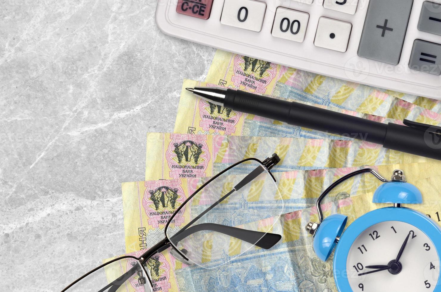 1 Ukrainian hryvnia bills and calculator with glasses and pen. Business loan or tax payment season concept. Time to pay taxes photo