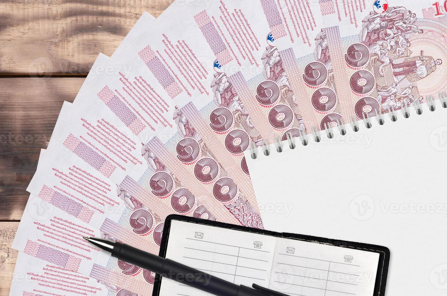 100 Thai Baht bills fan and notepad with contact book and black pen. Concept of financial planning and business strategy photo