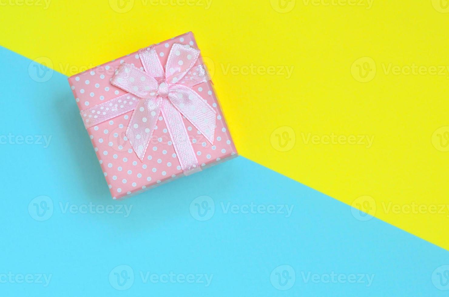 Small pink gift box lie on texture background of fashion pastel blue and yellow colors paper in minimal concept photo