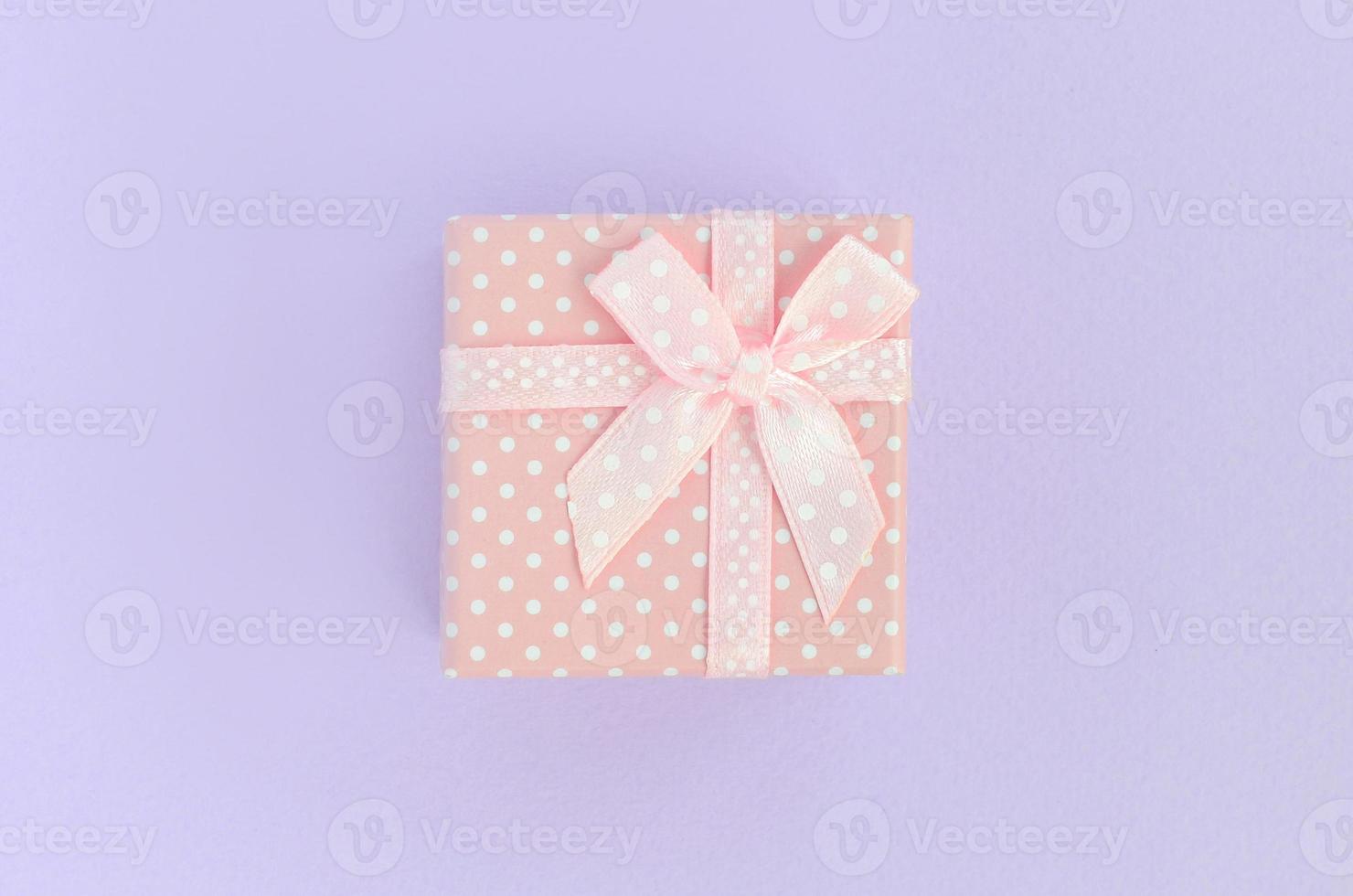 Small pink gift box with ribbon lies on a violet background. Minimalism flat lay top view photo