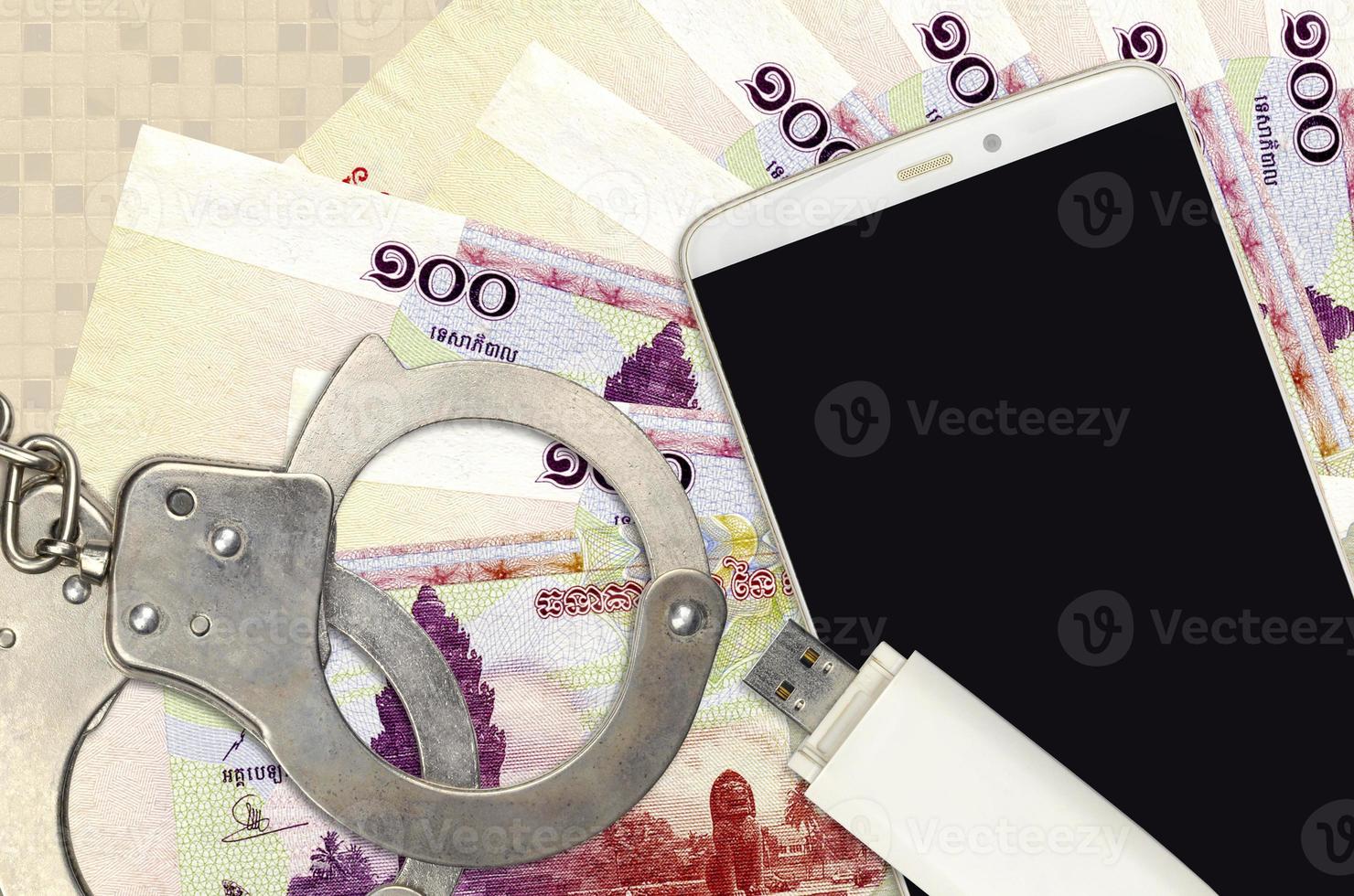 100 Cambodian riels bills and smartphone with police handcuffs. Concept of hackers phishing attacks, illegal scam or malware soft distribution photo