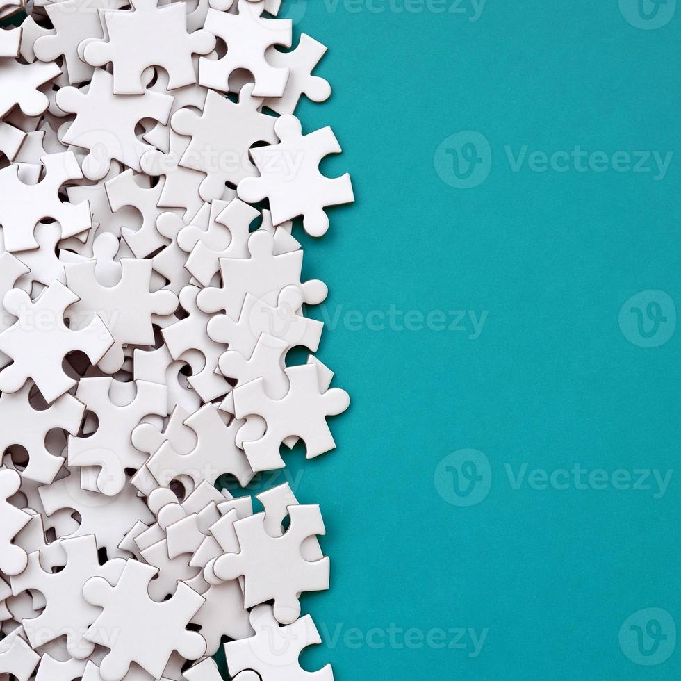 A pile of uncombed elements of a white jigsaw puzzle lies on the background of a blue surface. Texture photo with copy space for text