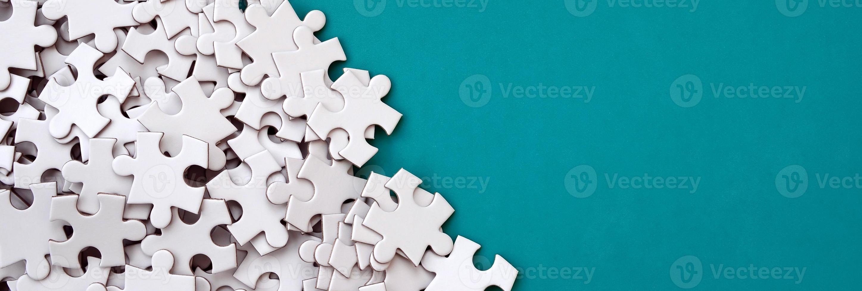 A pile of uncombed elements of a white jigsaw puzzle lies on the background of a blue surface. Texture photo with copy space for text