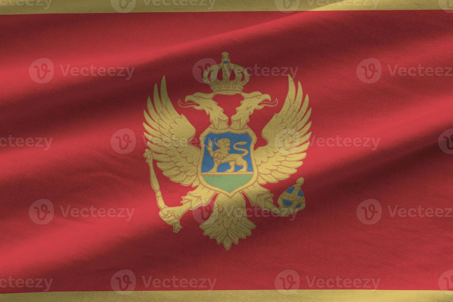 Montenegro flag with big folds waving close up under the studio light indoors. The official symbols and colors in banner photo