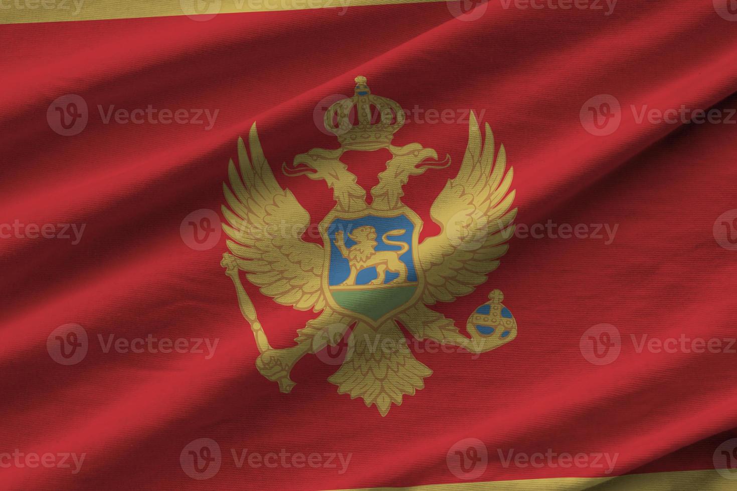 Montenegro flag with big folds waving close up under the studio light indoors. The official symbols and colors in banner photo