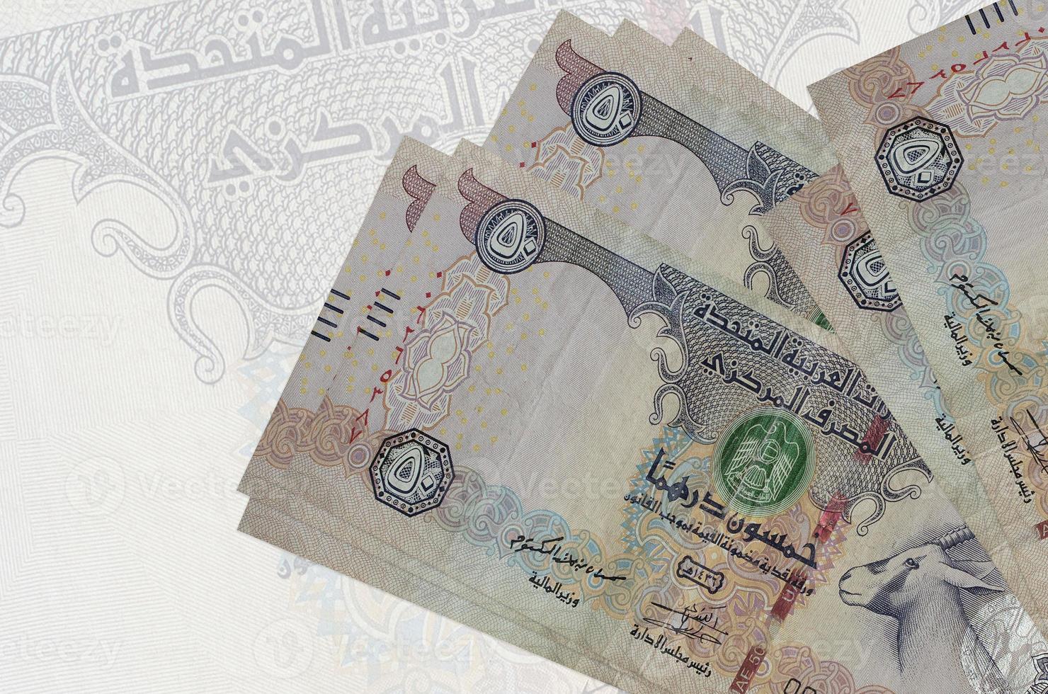 50 UAE dirhams bills lies in stack on background of big semi-transparent banknote. Abstract presentation of national currency photo