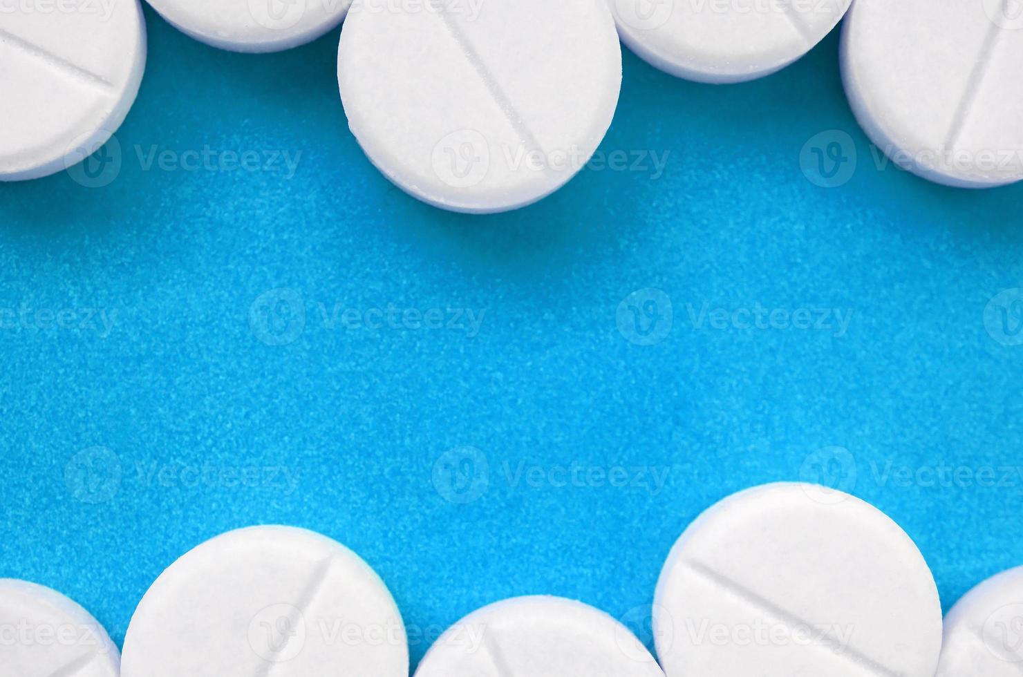 A few white tablets lie on a bright blue background surface. Background image on medical and pharmaceutical topics photo