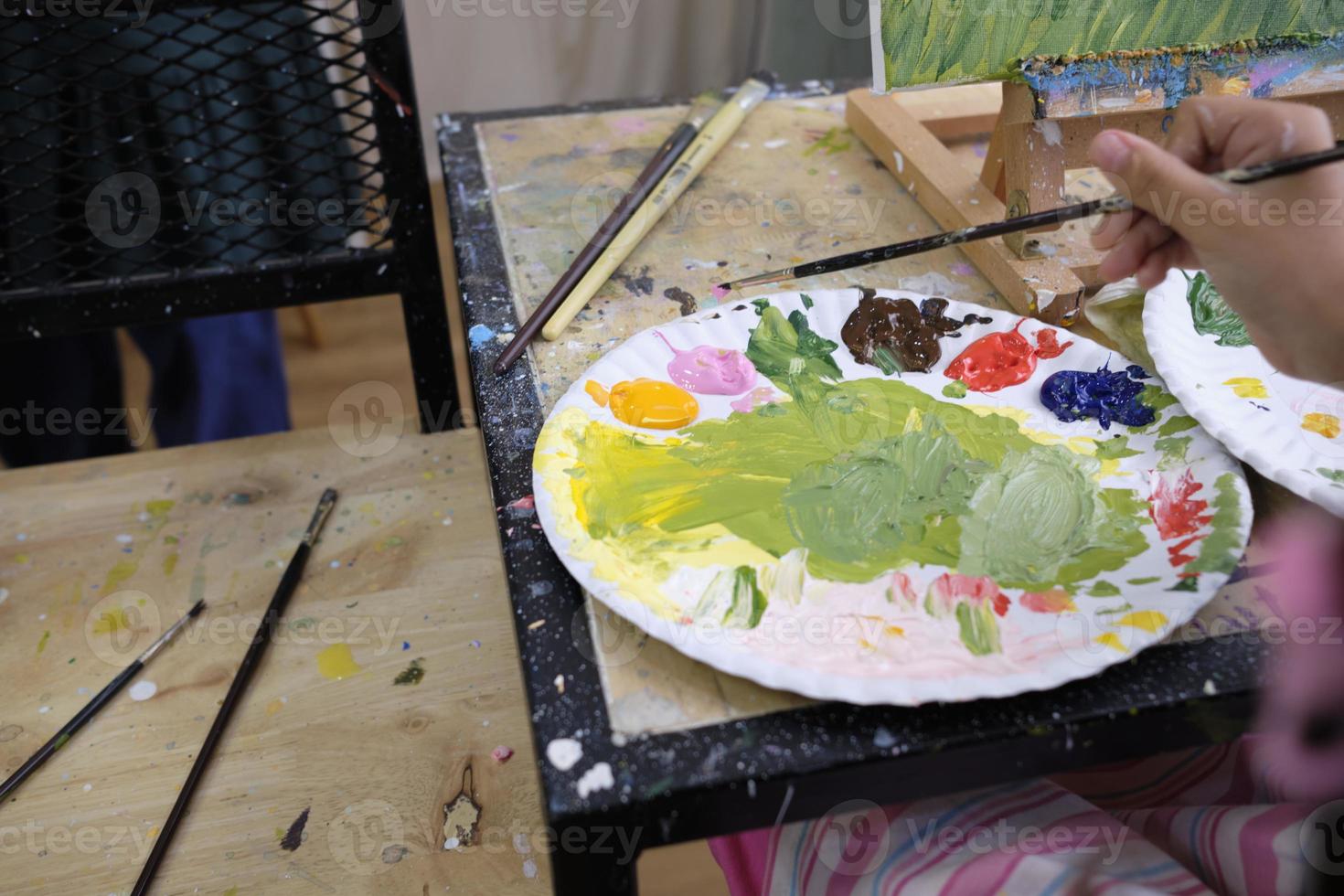 Close-up shot, acrylic colors palette, mixing and painting a picture by artist's hand, vivid multicolor in canvas with easel, colorful creativity with talent skills, artistic imagination design. photo