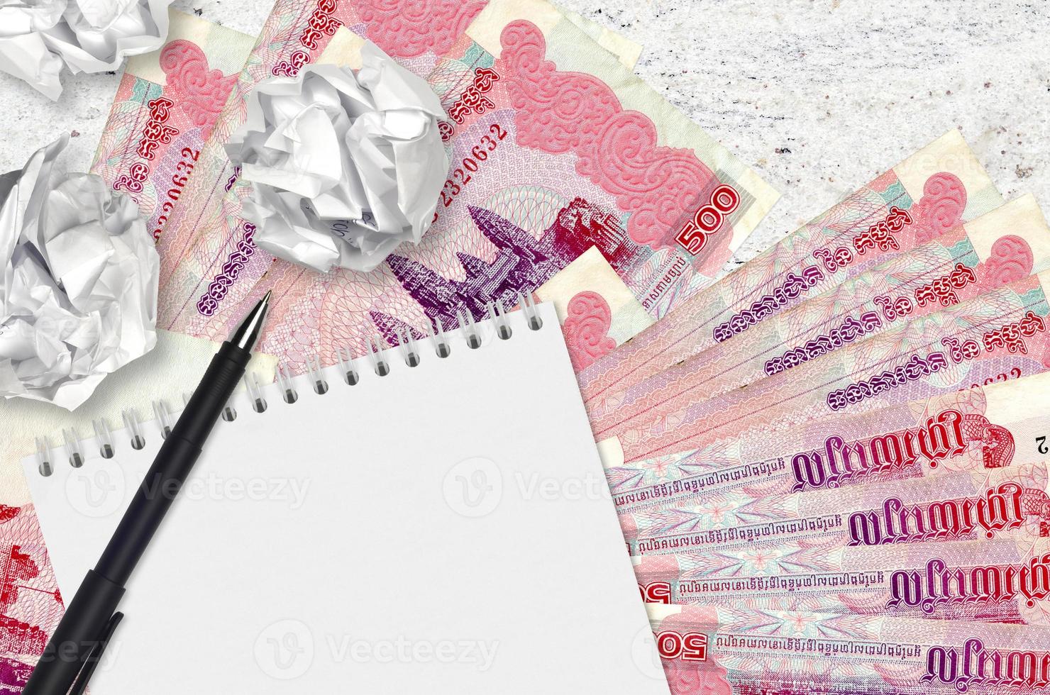 500 Cambodian riels bills and balls of crumpled paper with blank notepad. Bad ideas or less of inspiration concept. Searching ideas for investment photo