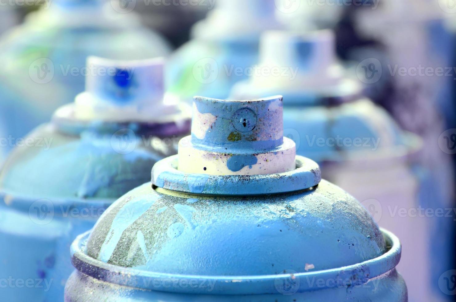 A lot of dirty and used aerosol cans of bright blue paint. Macro photograph with shallow depth of field. Selective focus on the spray nozzle photo