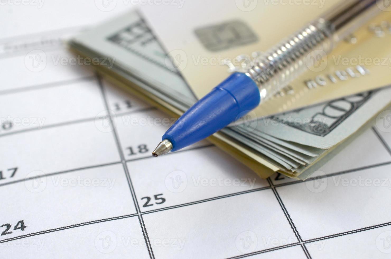 Pen and credit card on many hundred US dollar bills on calendar page close up photo