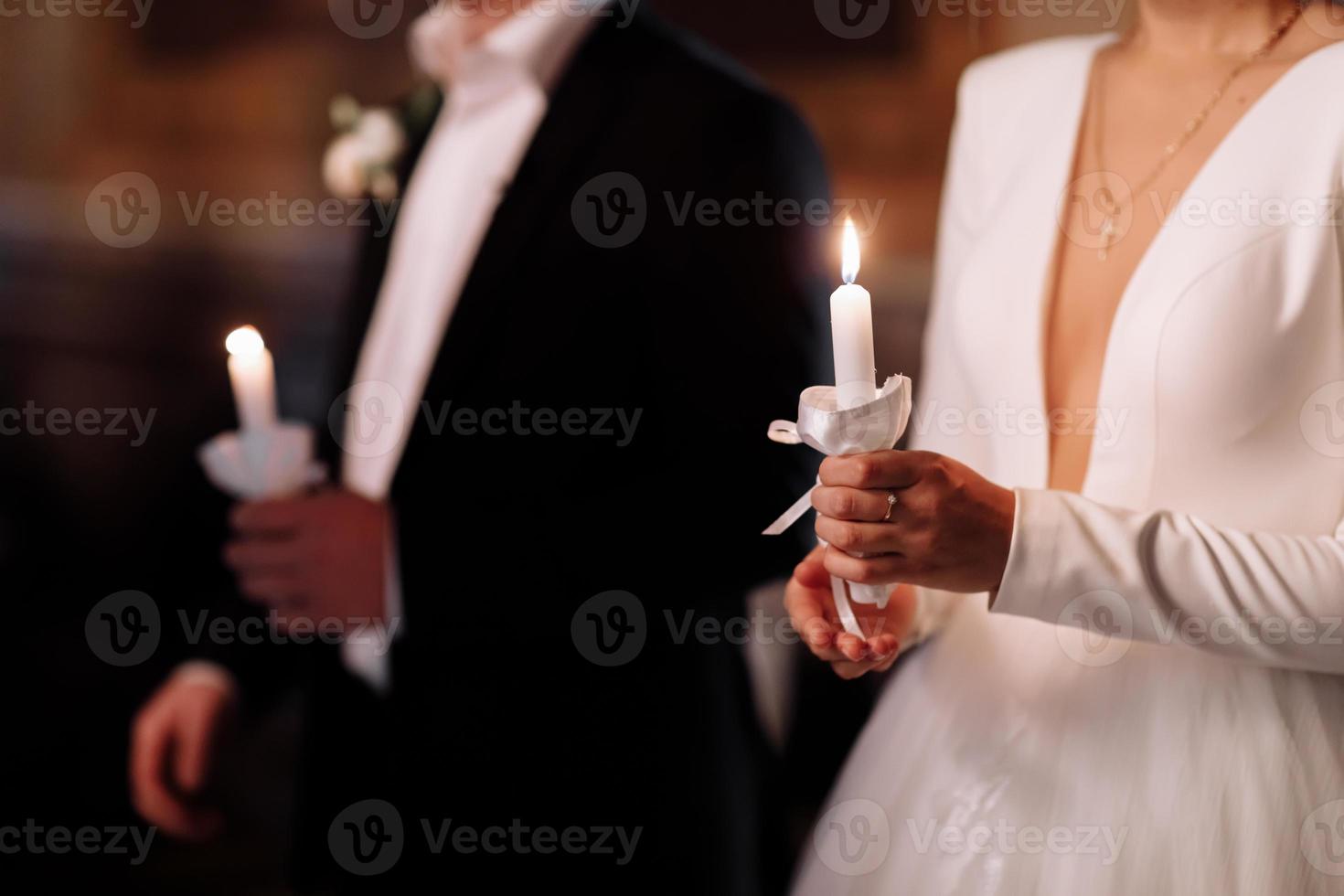 Couple in church. Bride and groom hold shiny candles during the ceremony in church. Hands of newlyweds with candles in church. Church religious details. Newlyweds swear to each other to love forever. photo