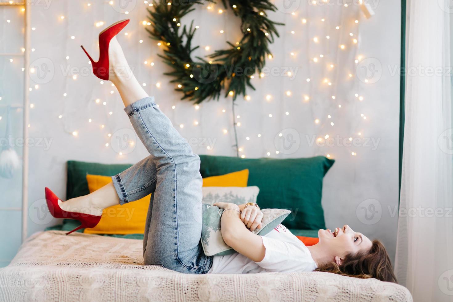 Portrait of gorgeous brunette woman in red high heels is having fun in bed and posing in the Christmas decorated interior. photo