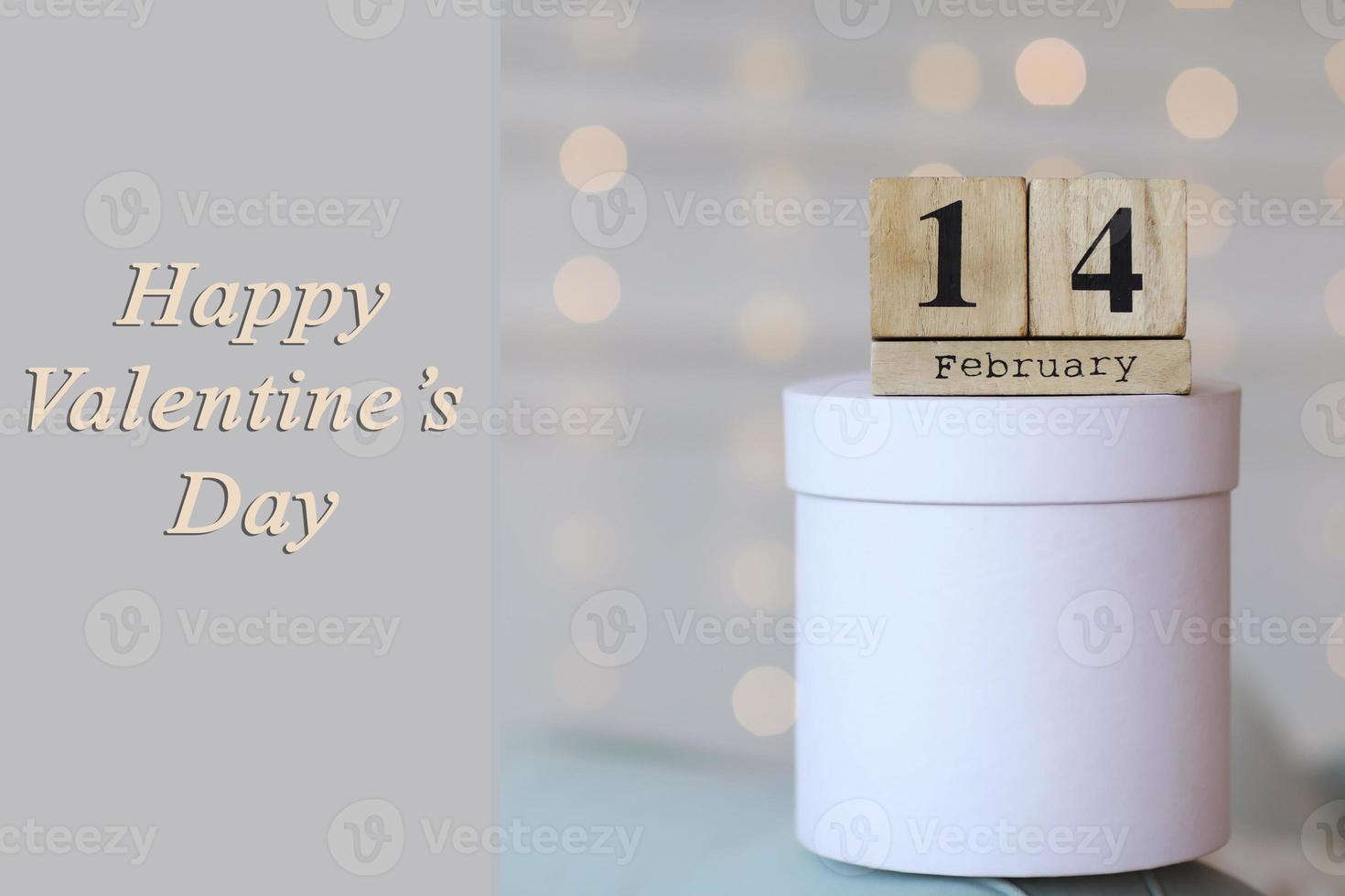 Valentine's day concept. Date 14 February on wooden red cube calendar on a white gift box. Bokeh golden and white background. photo