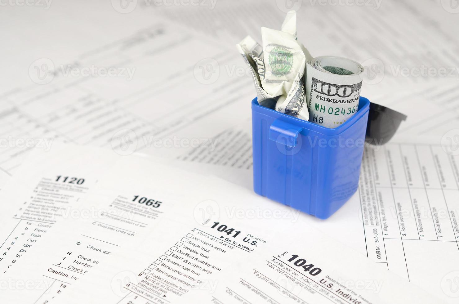 Many american tax blank forms and crumpled hundred dollar bill in trash bin photo