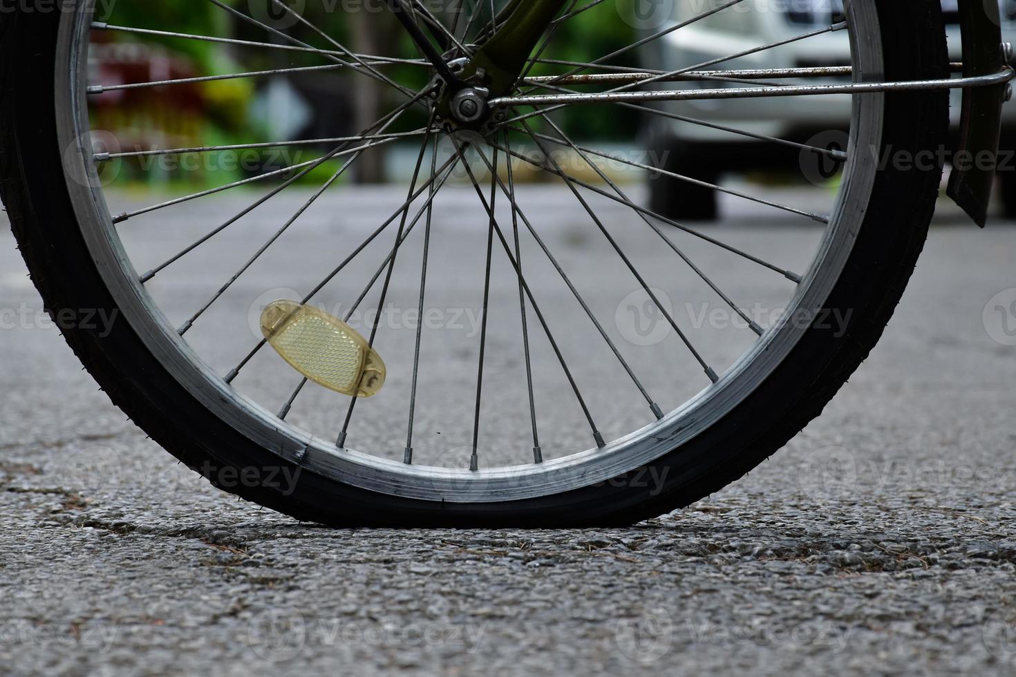 Rear wheel of bike which is flat and parked on the pavement beside the road. photo