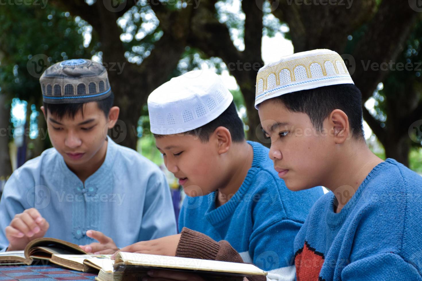 jóvenes asiáticos musulmanes o islámicos sentados juntos en el parque escolar para leer, aprender, hacer y consultar la tarea y esperando aprender temas religiosos en la escuela, enfoque suave y selectivo. foto