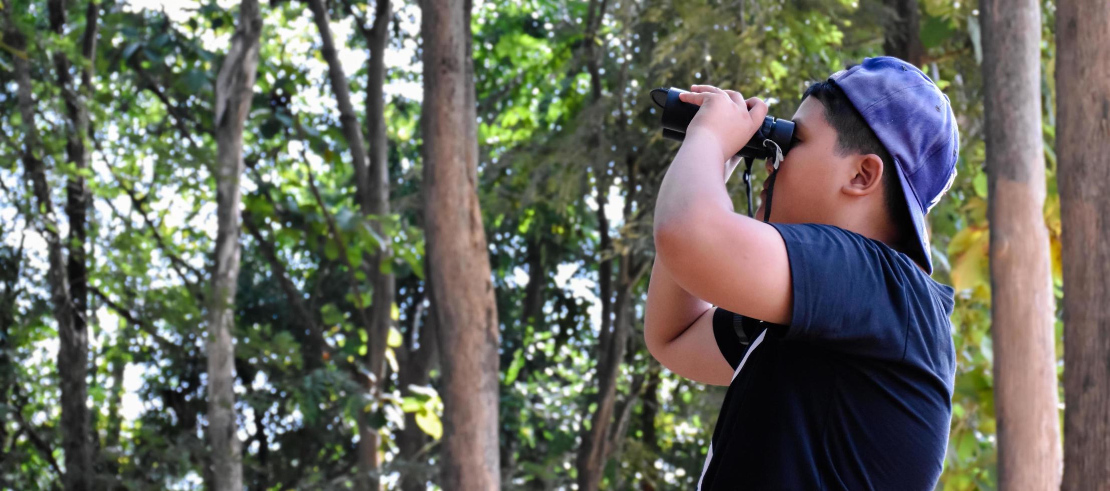 Southeast Asian boys are using binoculars to observe birds in tropical forest, idea for learning creatures and wildlife animals outside the classroom. photo