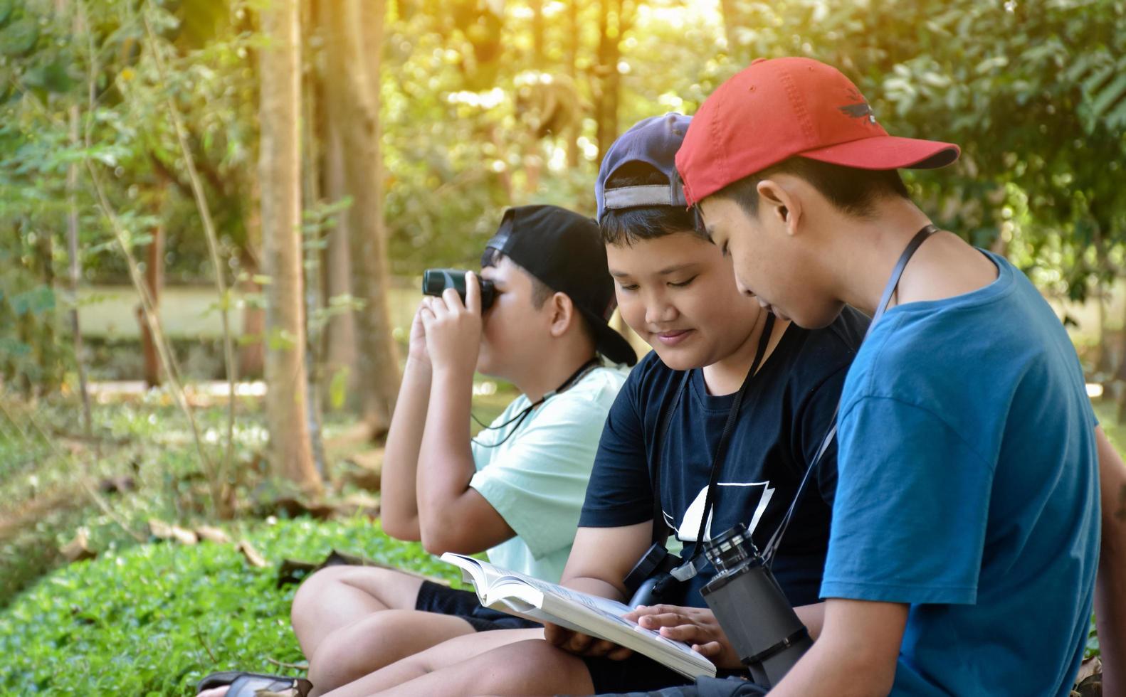 Southeast Asian boys are using binoculars to observe birds in tropical forest, idea for learning creatures and wildlife animals outside the classroom. photo