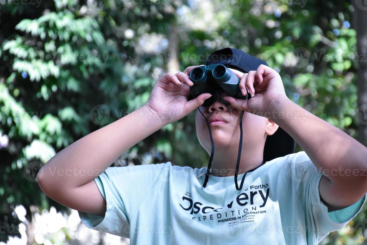 Southeast Asian boys are using binoculars to observe birds in tropical forest, idea for learning creatures and wildlife animals outside the classroom. photo