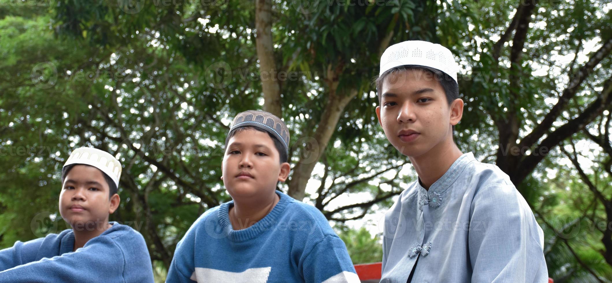 Young asian muslim or islamic boys sitting together in the school park to read, to learn, to do and to consult homework and waiting to learn religious subjects at school, soft and selective focus. photo