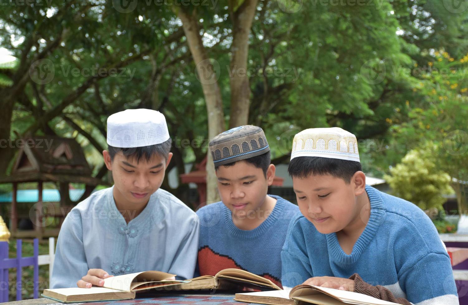 jóvenes asiáticos musulmanes o islámicos sentados juntos en el parque escolar para leer, aprender, hacer y consultar la tarea y esperando aprender temas religiosos en la escuela, enfoque suave y selectivo. foto