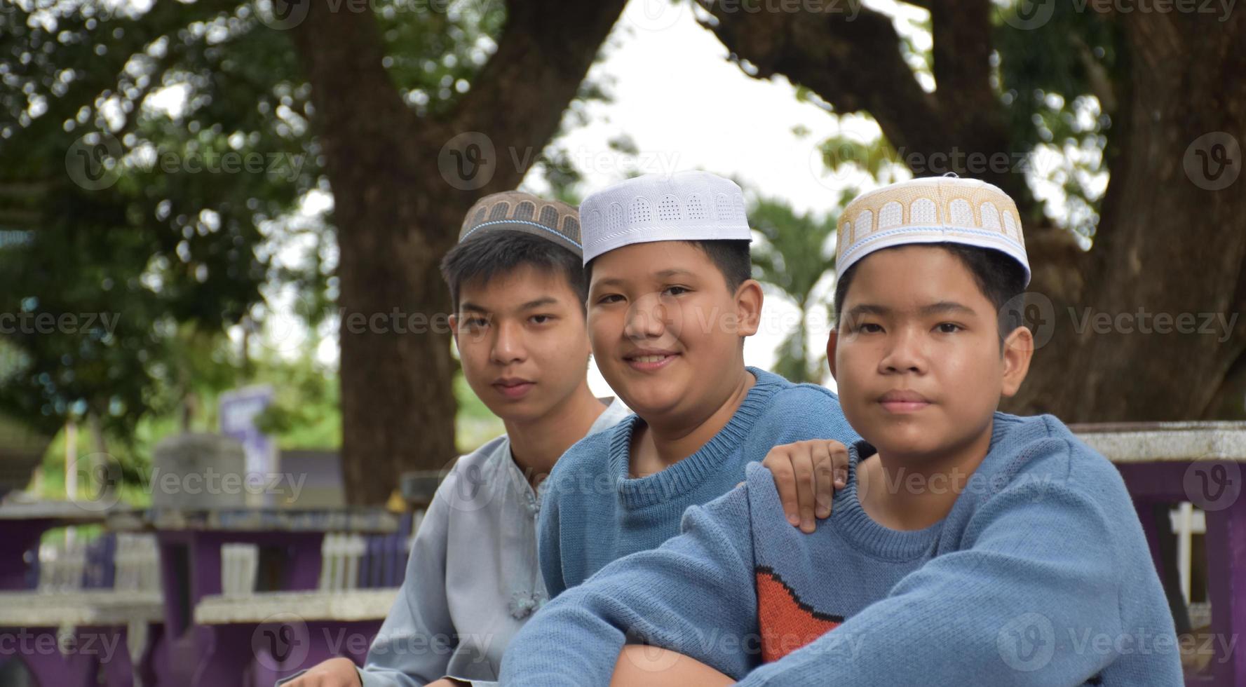 jóvenes asiáticos musulmanes o islámicos sentados juntos en el parque escolar para leer, aprender, hacer y consultar la tarea y esperando aprender temas religiosos en la escuela, enfoque suave y selectivo. foto