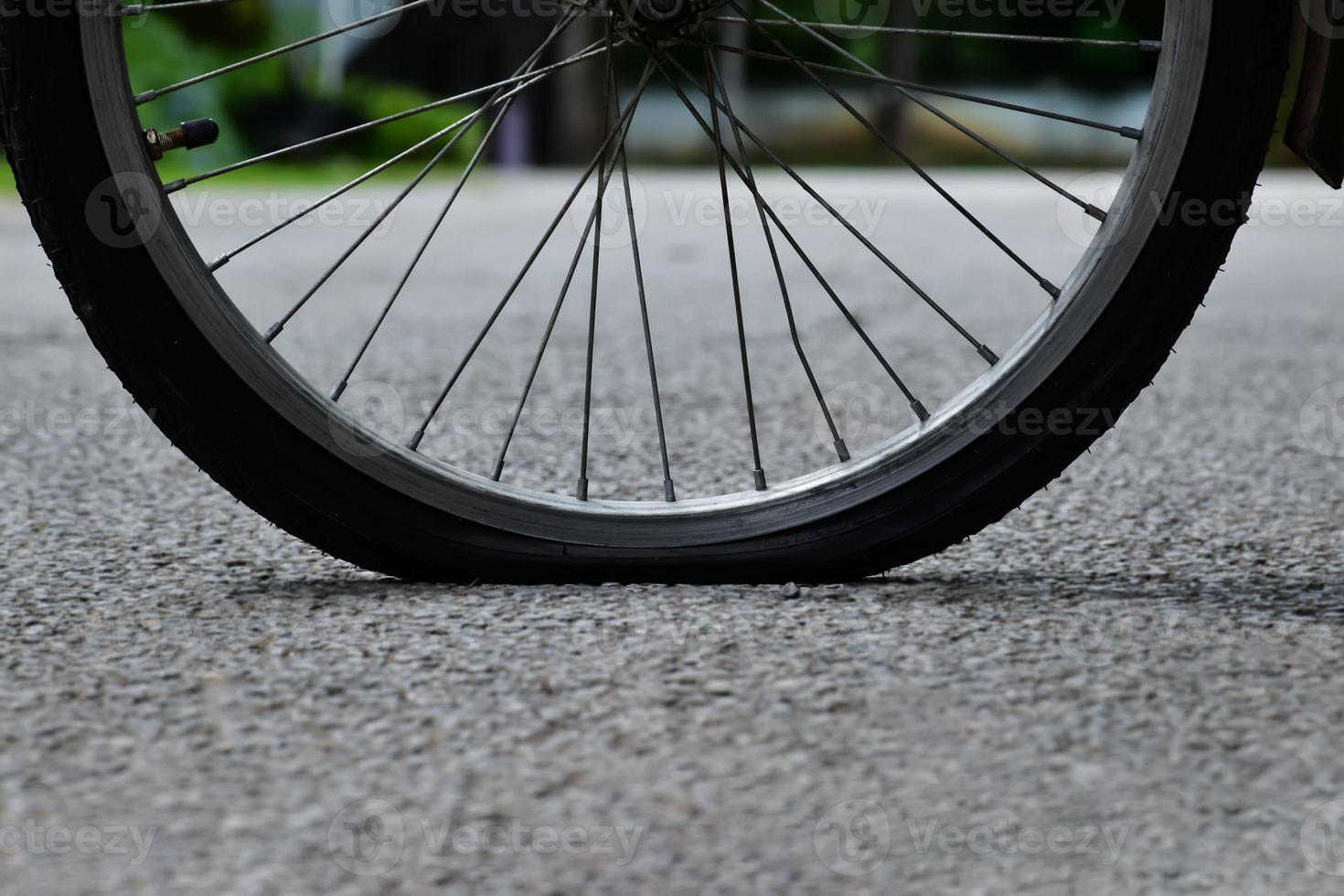 Rear wheel of bike which is flat and parked on the pavement beside the road. photo