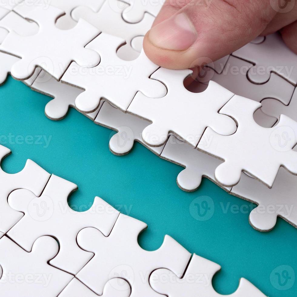 The human hand paves the way to the surface of the jigsaw puzzle, forming a blue space. The concept of overcoming the difficulties on the way to success photo